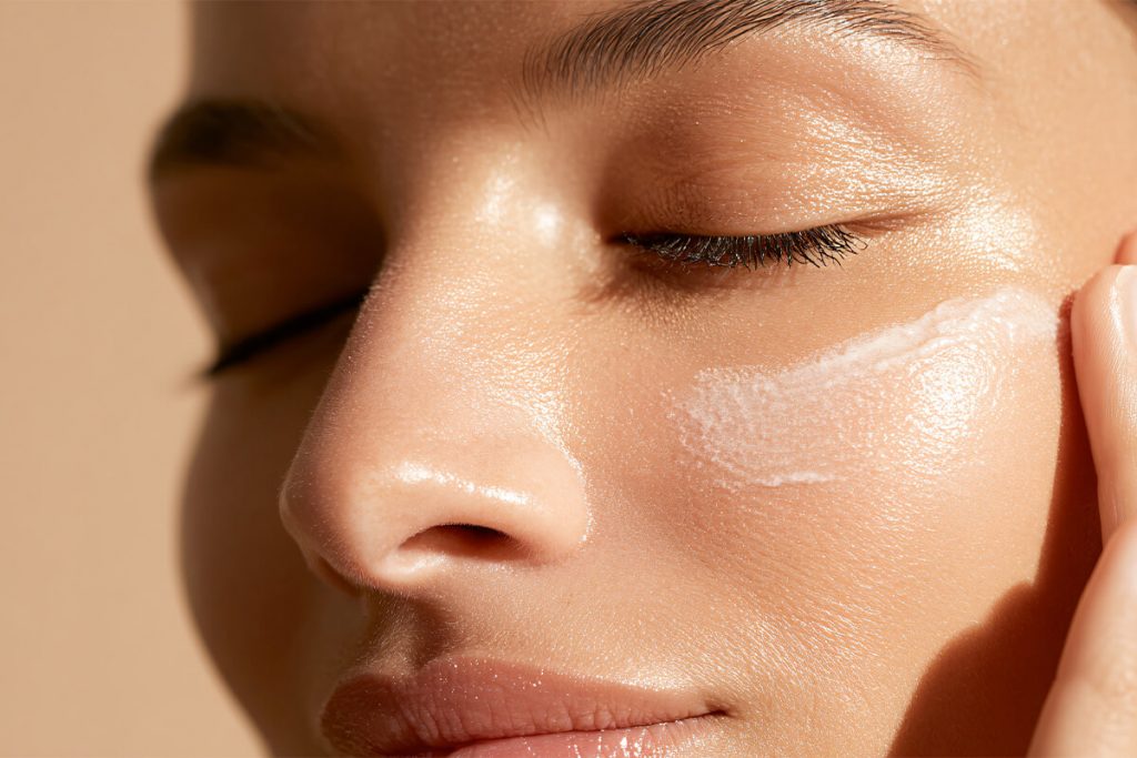 Nahaufnahme von Frauengesicht beim Auftragen von Gesichtscreme.