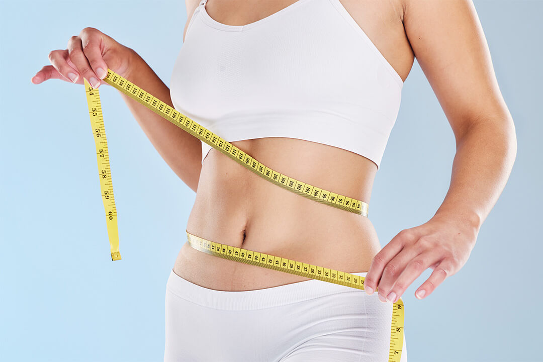 Person misst ihre Taille mit einem Maßband über Sportkleidung.