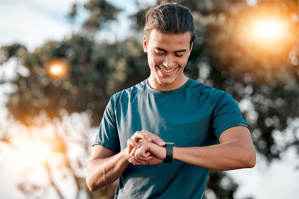Junger aktiver Mann schaut auf Smartwatch und lächelt.