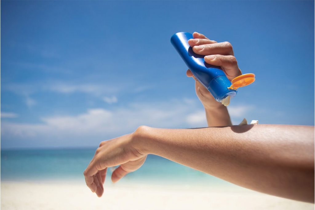 Person trägt am Strand Sonnenschutzcreme auf den Arm auf..